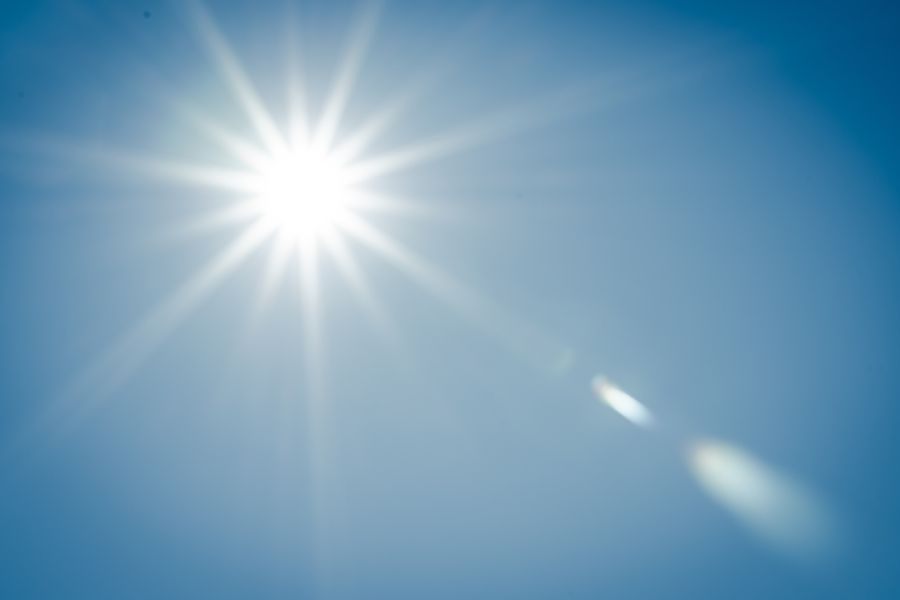 An image of the sun in the sky and the rays reflecting off the lens of the camera.