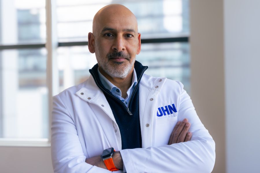 Dr. Jaideep Bains wearing a white research coat with a UHN logo stitched into it. His arms are crossed and he is slightly smiling. 