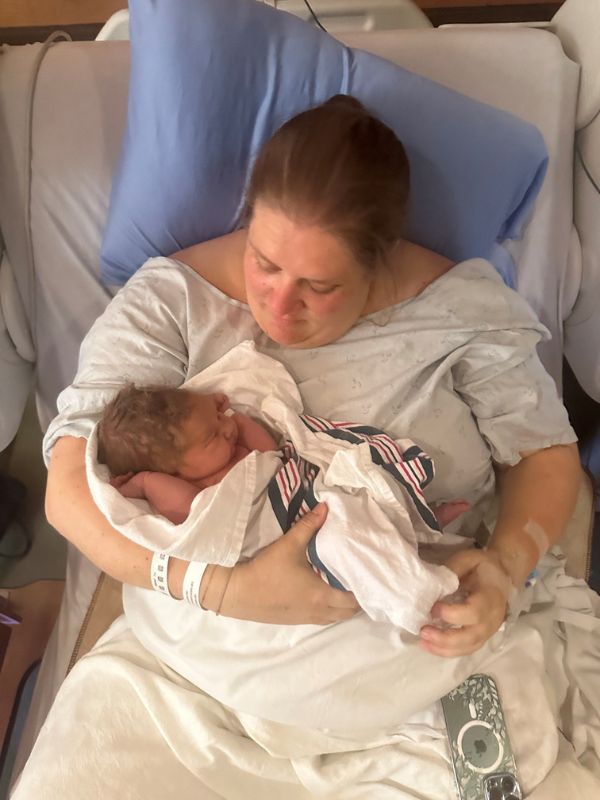 Sarah O'Born holding her daughter while resting in a hospital bed with hospital linen wrapped around both of them.