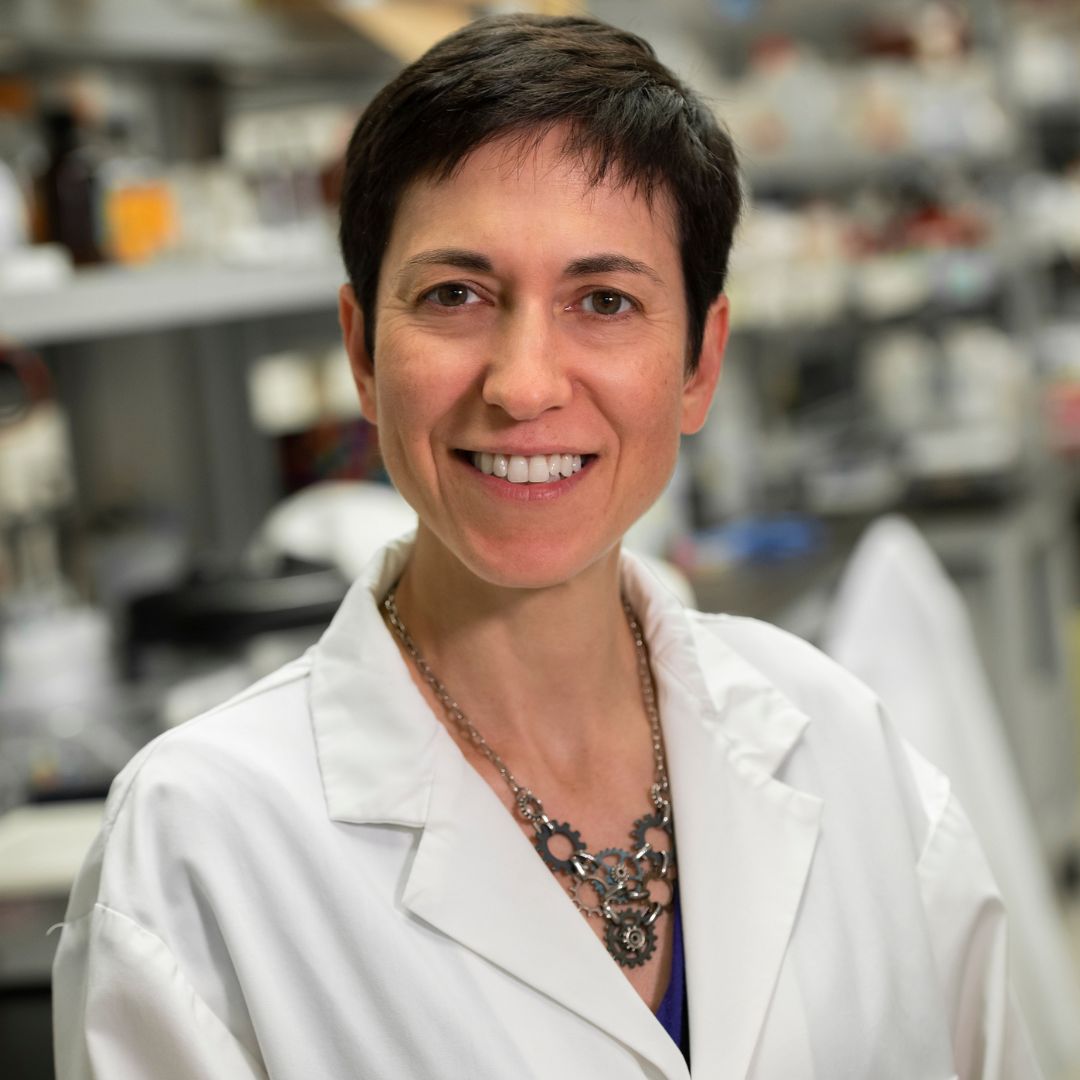 Dr. Carmela Tartaglia wearing a white research coat and smiling while in the lab.