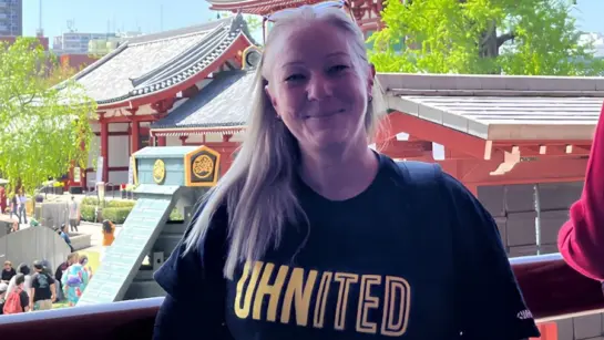 Claire Thomas standing next to a temple in Japan while wearing her black and yellow UHNITED t-shirt.