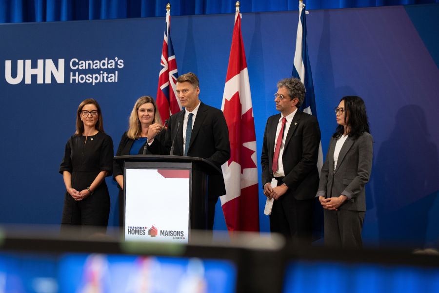 Gregor Robertson is speaking at the podium while four others watch from on stage as he speaks.