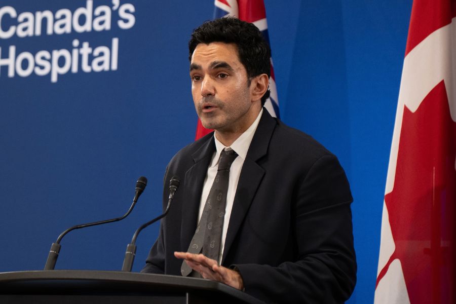 Dr. Andrew Boozary at a podium speaking about how housing is health care. Behind him is the Canadian flag.