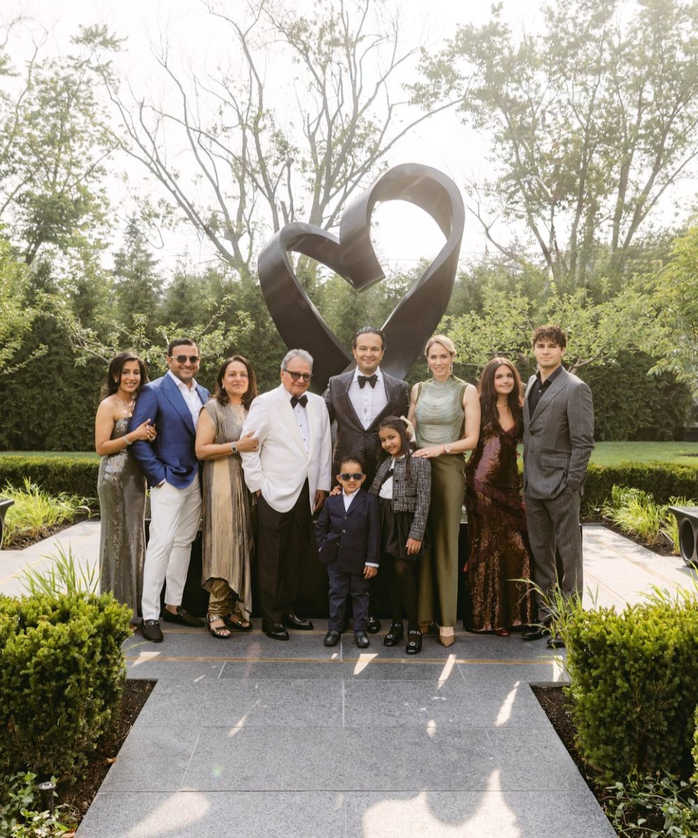 Ten members of the Ajmera family standing in front of a heart statue and garden.